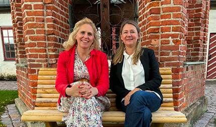 Kamilla Thue och Hanna Andersson på bänk framför gammal byggnad